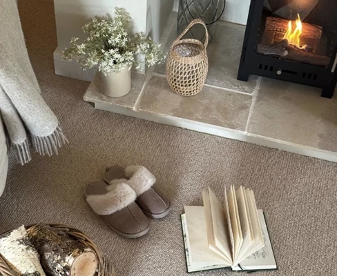 Beige wool carpet by a fireplace with slippers and book